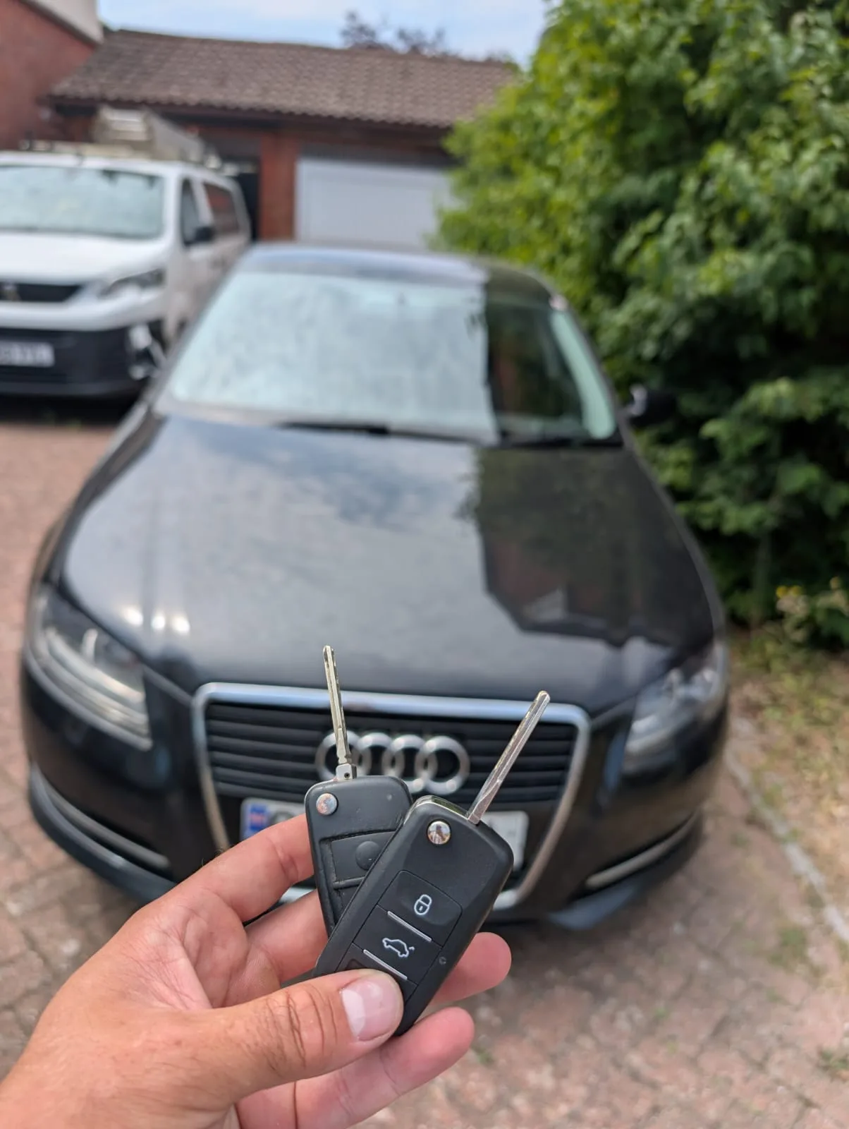 Two Audi A3 flip keys held up in front of a dark grey Audi A3 on a residential driveway in Milton Keynes