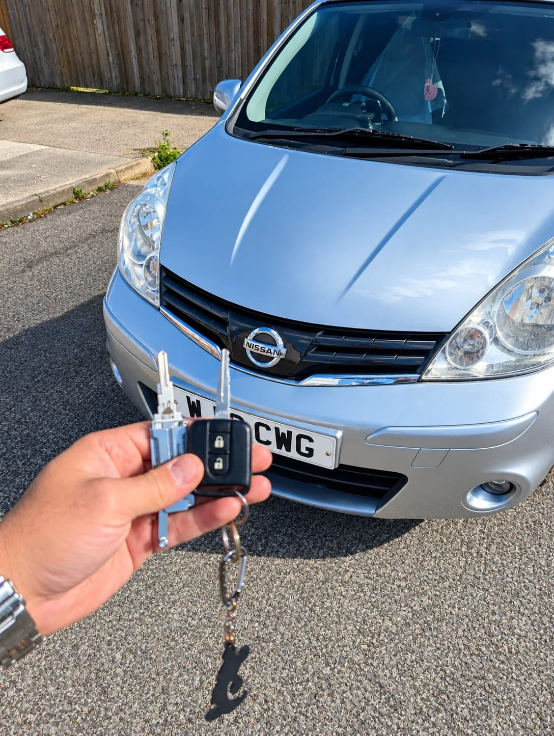 Two Nissan Note flip keys held up in front of a silver Nissan Note 2012 after emergency opening in Northampton